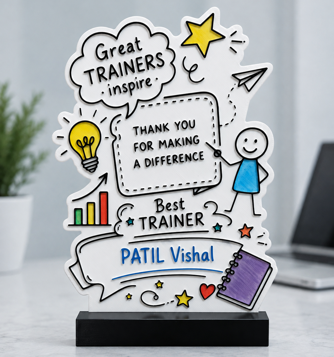 A custom cartoon-style acrylic award plaque on a black base, featuring hand-drawn illustrations and text celebrating a trainer named Patil Vishal, displayed on a light marble surface with a blurred office background.